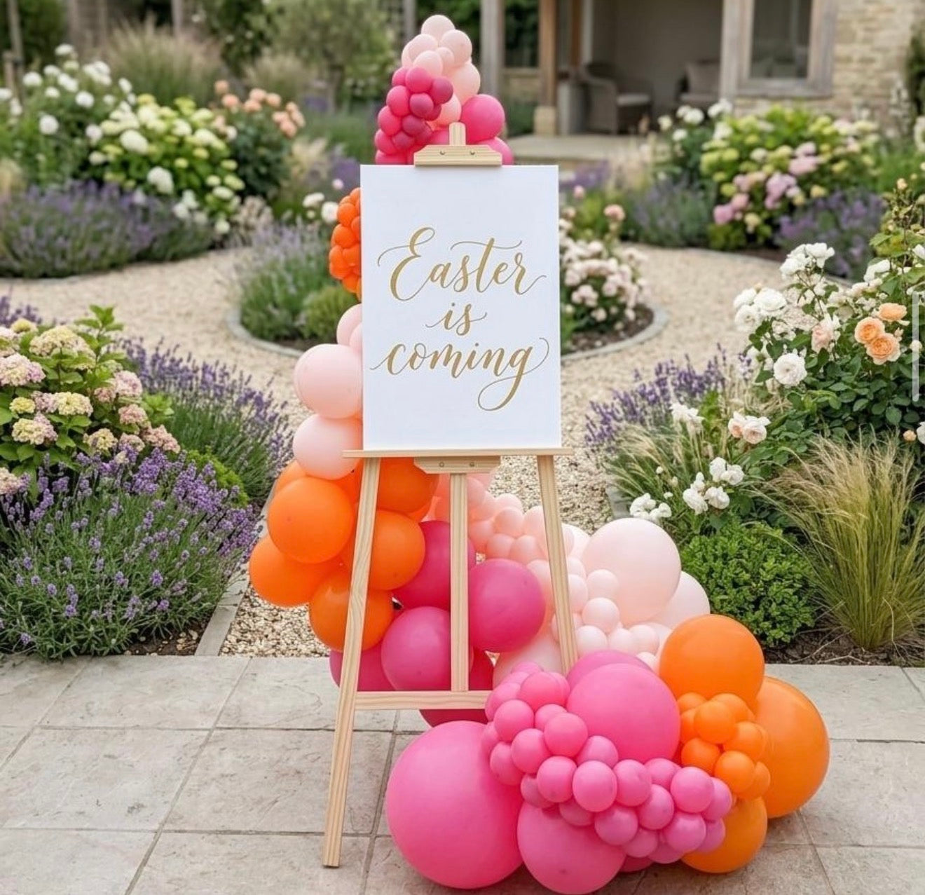 Decorative setup with balloons and a sign reading 'Easter is coming' in a garden.
